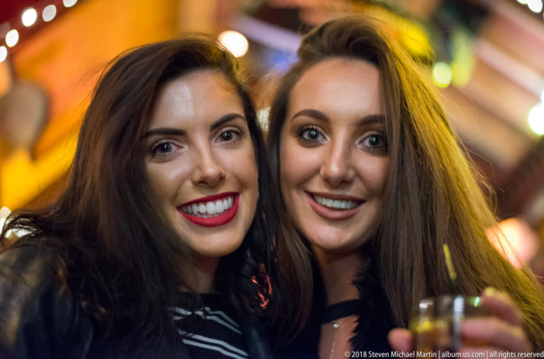 Two smiling women posing together in a crowded Galway pub, with warm lights and other patrons blurred behind them.