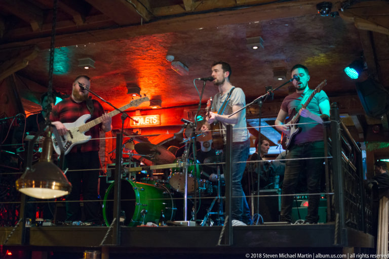 Four-piece band with guitars, drums, and microphones performing on a compact Galway pub stage.