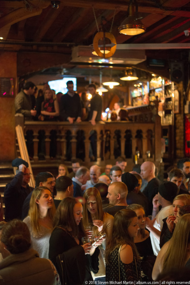 Crowded two-level Galway pub with patrons on the main floor and an upper gallery behind a wooden balustrade.