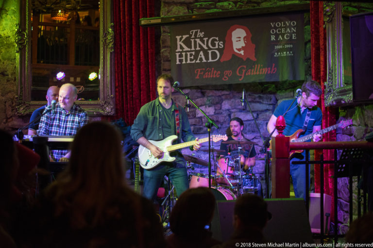 Band performing against a stone wall beneath a “The Kings Head” banner reading “Fáilte go Gaillimh.”