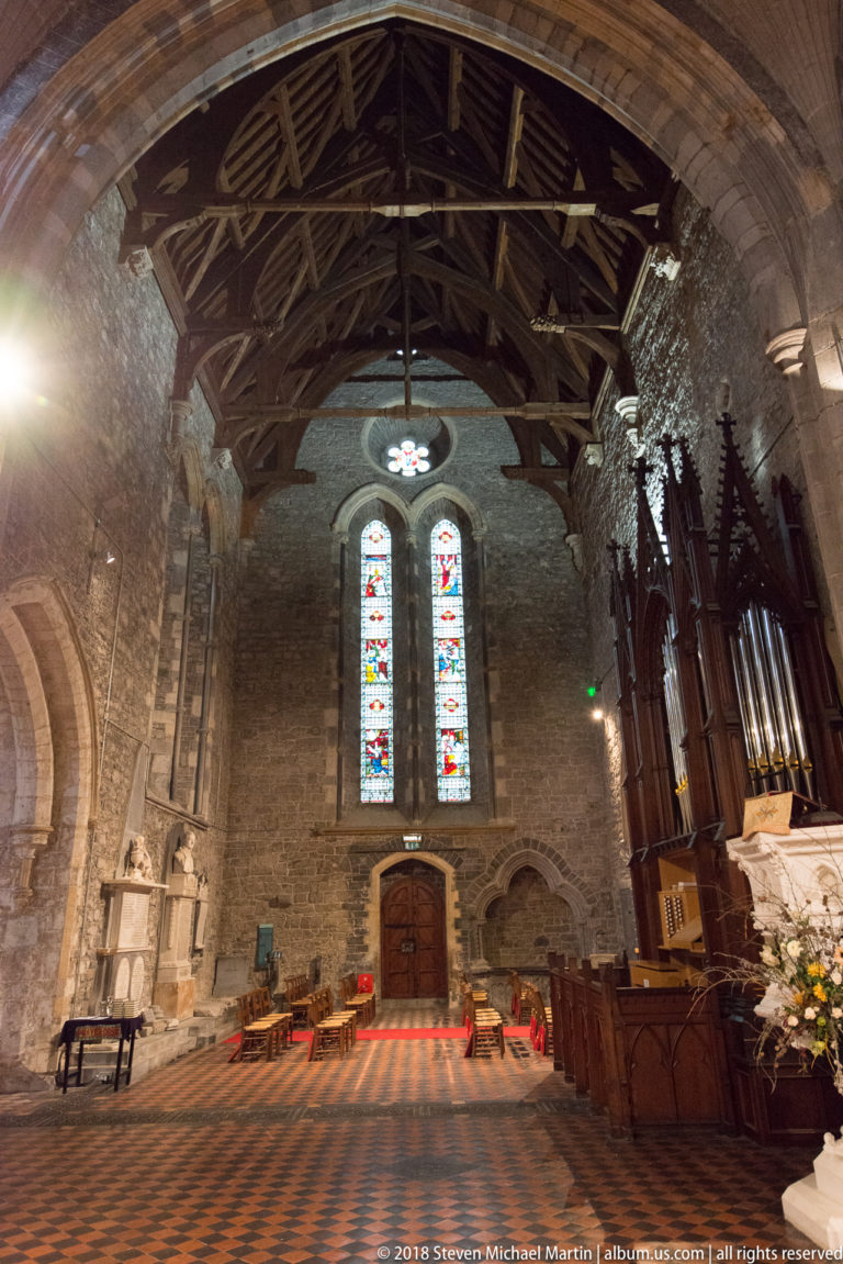 Cathedral interior with pipe organ, stained-glass windows, timber roof and patterned tile floor.