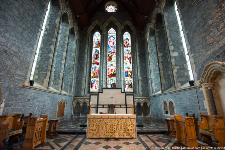 Altar centered beneath three stained-glass lancets in the stone eastern end of St Canice’s Cathedral.