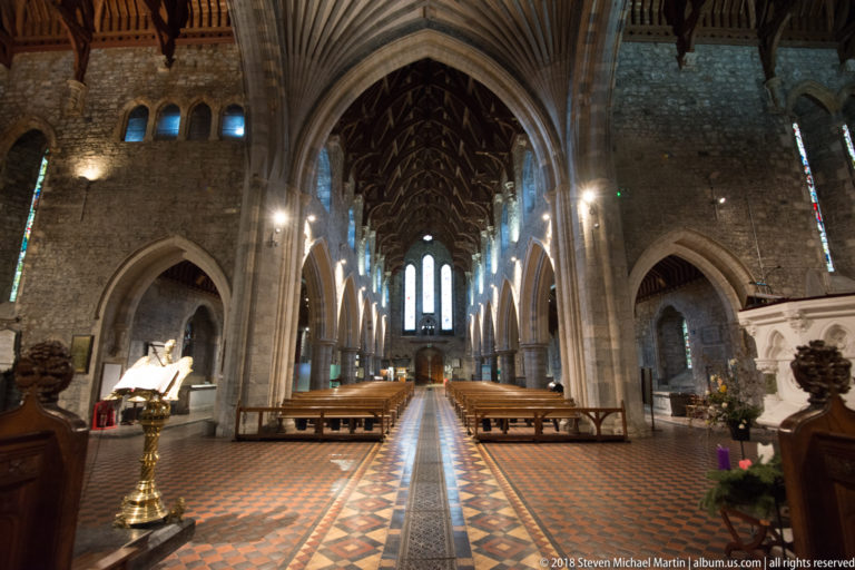 Long nave view with patterned central aisle, pointed arches, timber roof, brass lectern and side monuments.