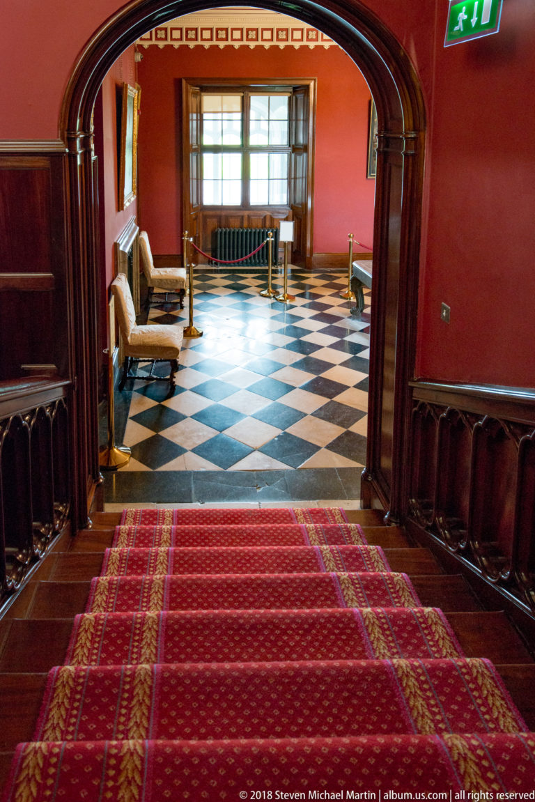Dark arched doorway leading from red carpet into a room with a black-and-white checkerboard floor.