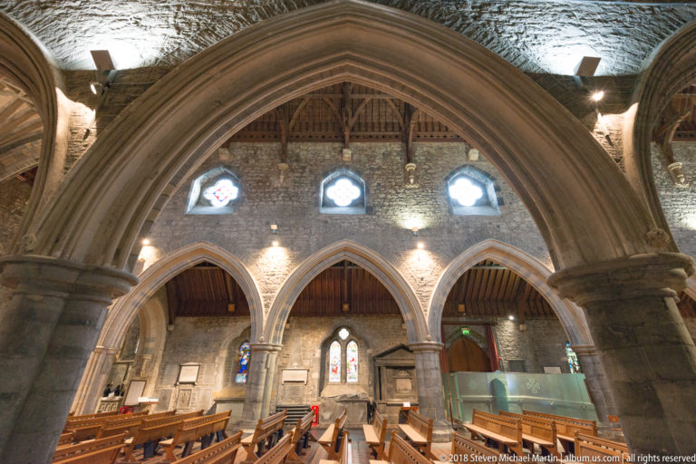 Large pointed stone arch framing three smaller arches, pews and wall memorials inside St Canice’s Cathedral.