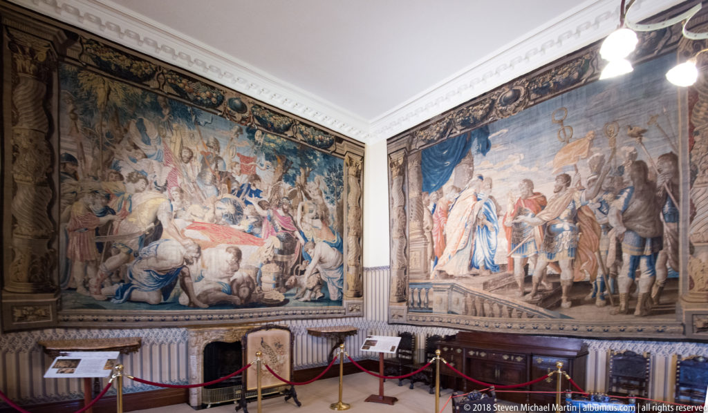 Two large historic tapestries covering adjacent walls in a gallery with display barriers and interpretive labels.