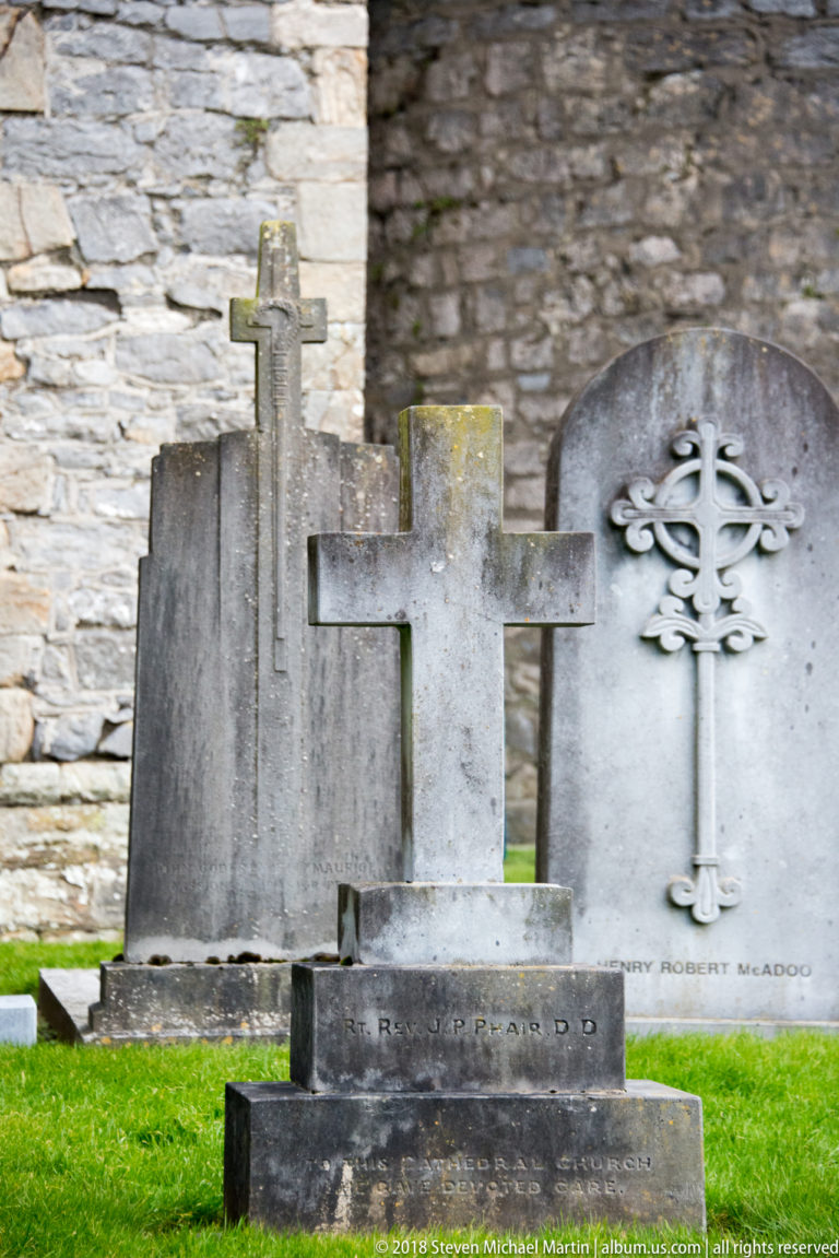 Cluster of weathered stone grave markers, including plain crosses and an openwork cross headstone.