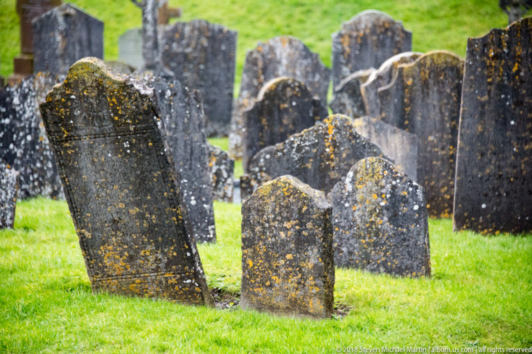 Lichen-covered headstones, some leaning, stand in bright grass with more grave markers behind.