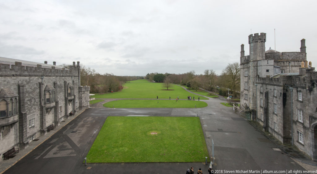 Elevated view between Kilkenny Castle ranges toward a rectangular lawn, curving paths, and parkland.