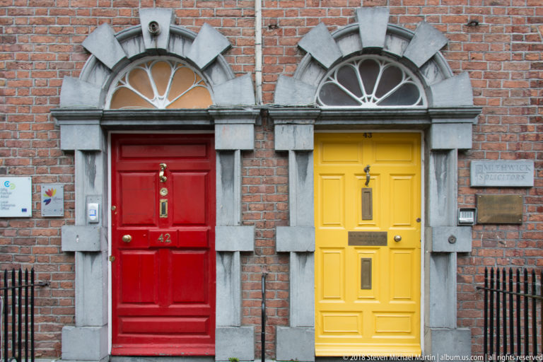 Red and yellow paneled doors with fanlights set side by side in a red-brick façade with gray stone trim.