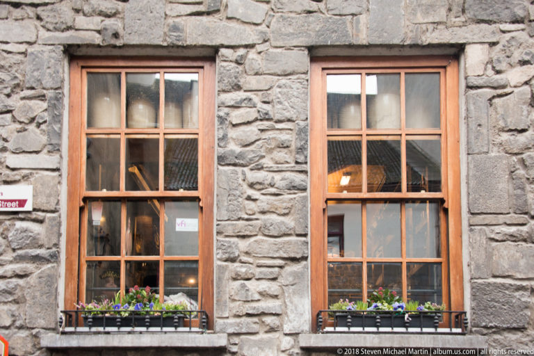 Two tall wooden sash windows with flower boxes set into a rough gray stone wall.