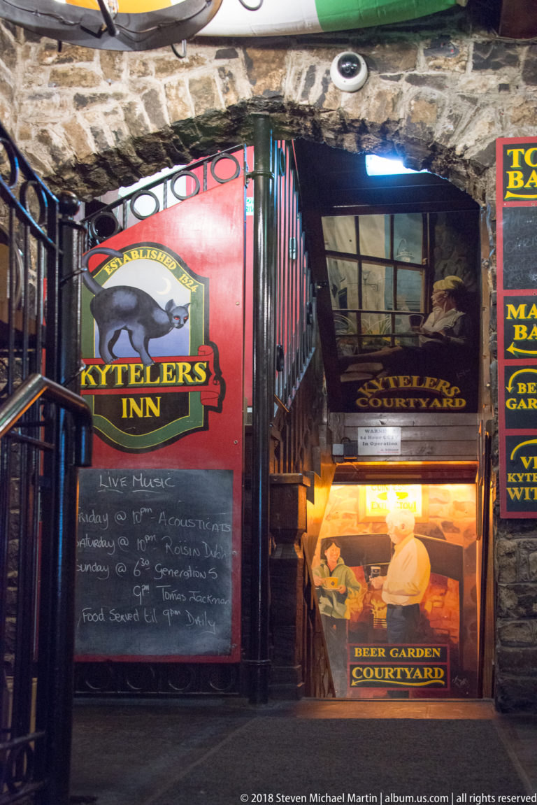 Stone interior at Kyteler’s Inn with stair railings and colorful signs for live music and the courtyard beer garden.