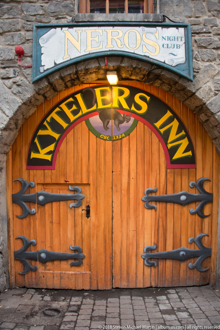 Arched wooden Kyteler’s Inn doorway with large black decorative strap hinges and painted lettering above the entrance.