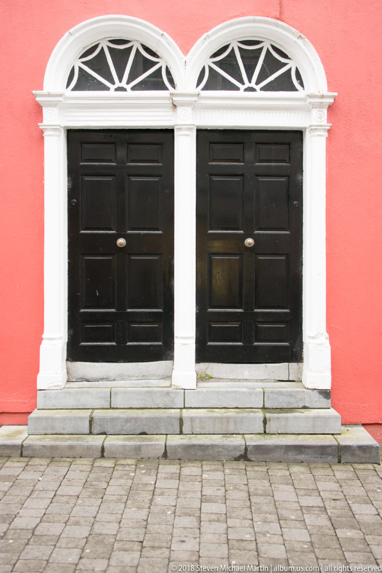 Two black paneled doors with white semicircular fanlights and trim set in a bright red stucco wall.