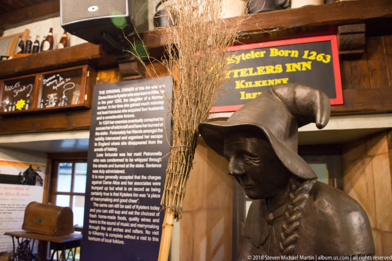 Dark pointed-hat figure beside an interpretive panel about the original owner of Kyteler’s Inn.