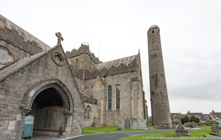 Pointed stone entrance to St Canice’s Cathedral, with lancet windows and the round tower visible beyond.