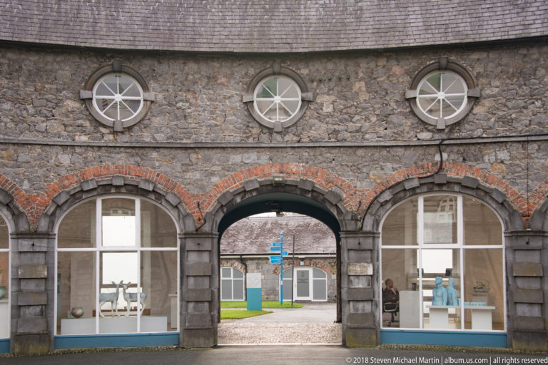 Three stone arches outlined in red brick beneath circular windows, with a central passage opening into another courtyard.