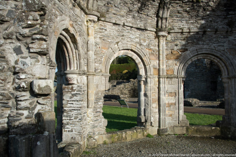 Three adjoining stone arches in a ruined abbey wall, including a narrow pointed doorway and larger round-headed openings.