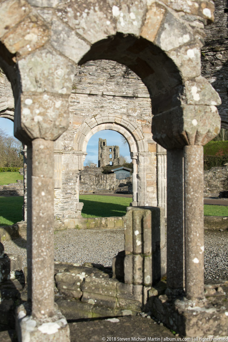 View through several aligned stone arches, framing additional ruined walls and a distant rectangular opening across the abbey grounds.