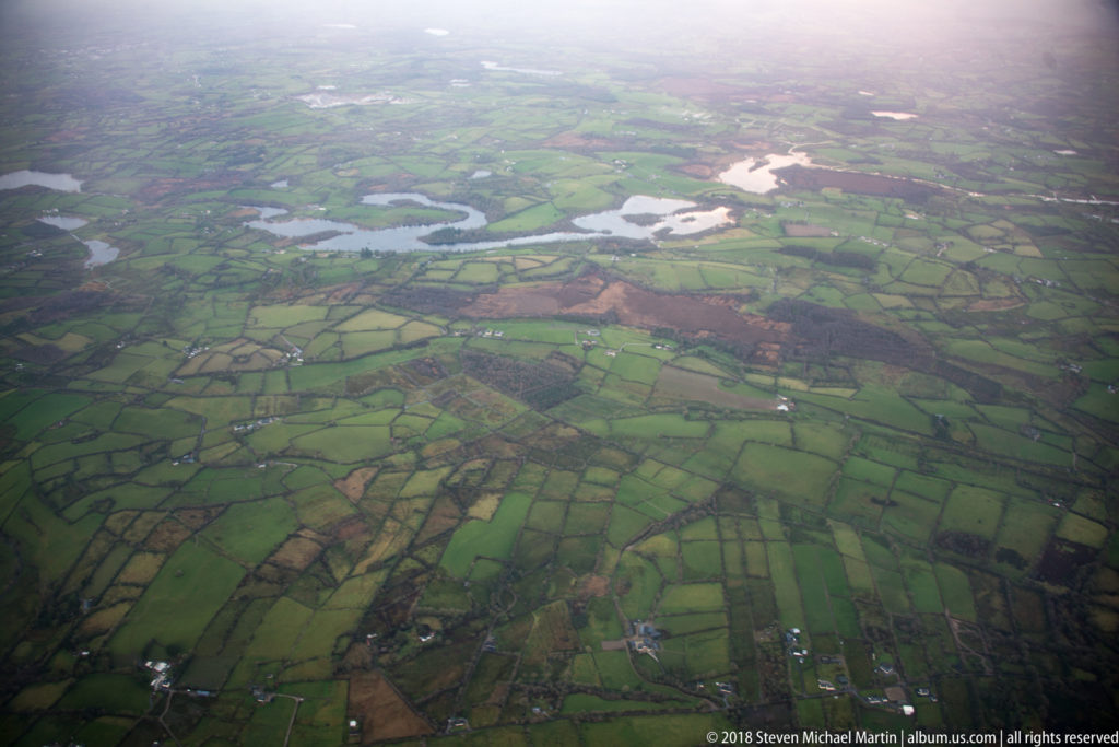 Patchwork green fields, hedgerows, scattered houses, and winding waterways seen from high above rural County Kerry.