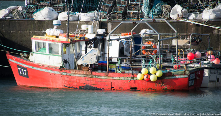 Red fishing boat moored beside a quay, with yellow and orange buoys hanging along the rail.