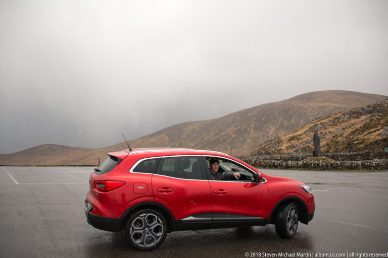 Red SUV stopped on an empty upland road, with the driver visible and brown hills behind.