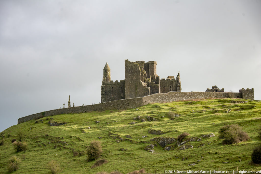 Rock of Cashel towers and walls above a sloping green hill with exposed limestone outcrops.