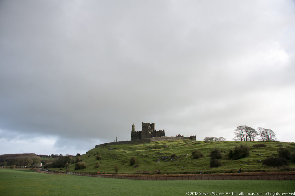 Distant Rock of Cashel on a green hill beneath dramatic dark storm clouds.