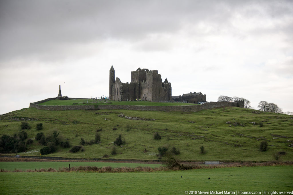 Rock of Cashel on a broad green hill viewed across open farmland under an overcast sky.