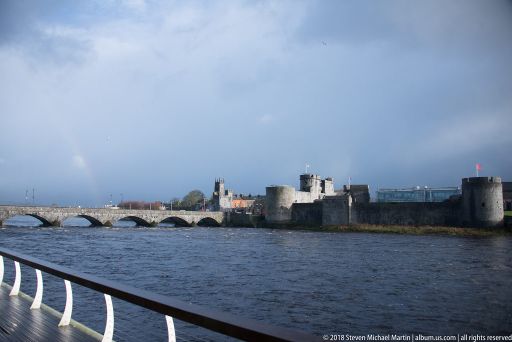 Wide view of King John’s Castle and Thomond Bridge across the River Shannon with a faint rainbow at left.