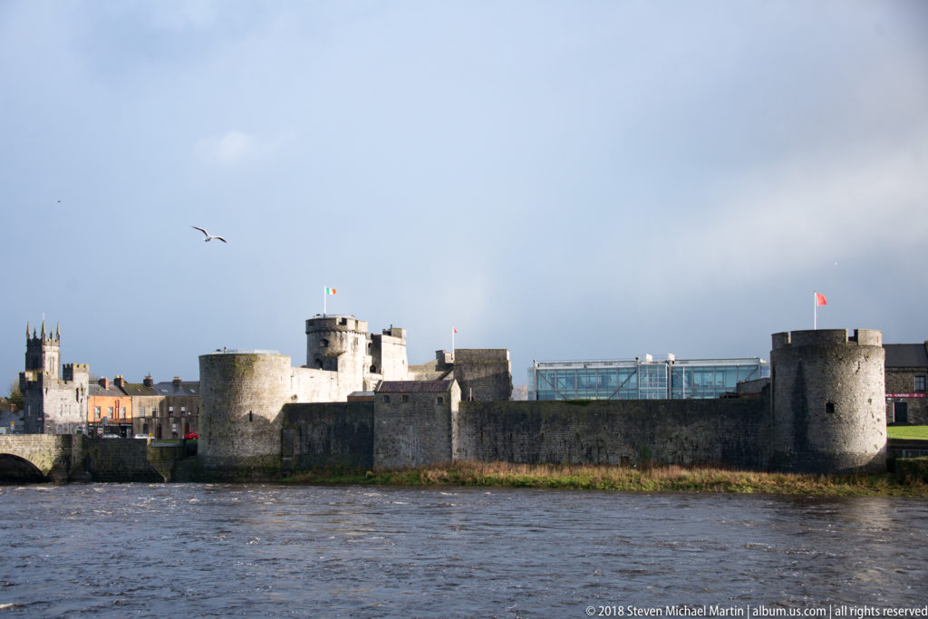 King John’s Castle viewed across the River Shannon, with round towers, stone walls, and a modern glazed structure.