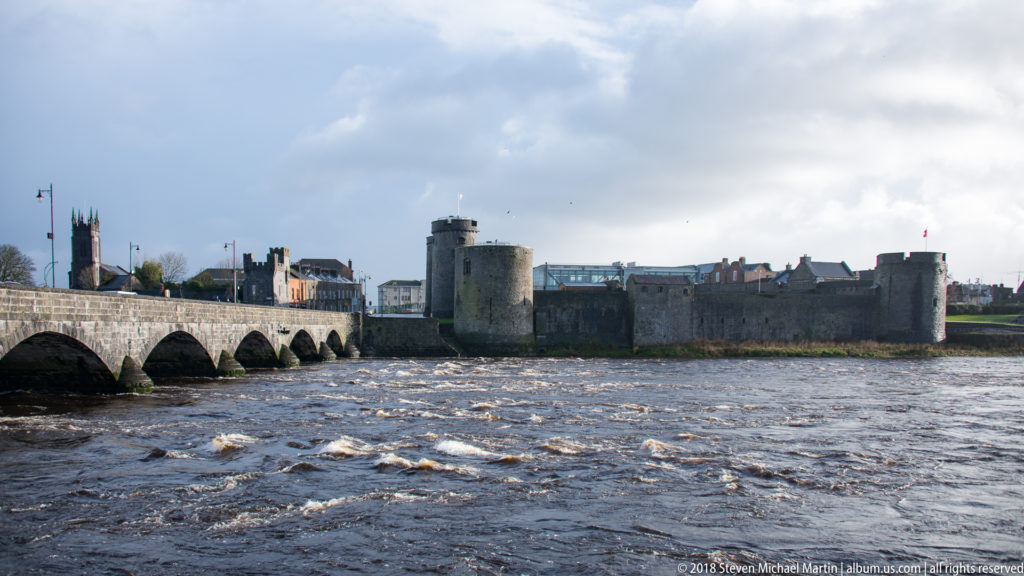 Thomond Bridge spans the River Shannon toward King John’s Castle with Limerick buildings and church towers behind.