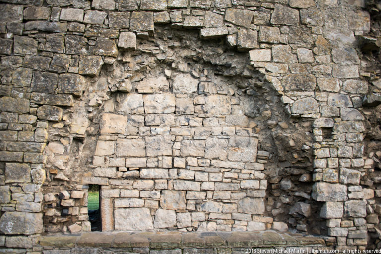 Large arched recess in rough stone masonry filled with later stonework, leaving a small rectangular opening near the base.