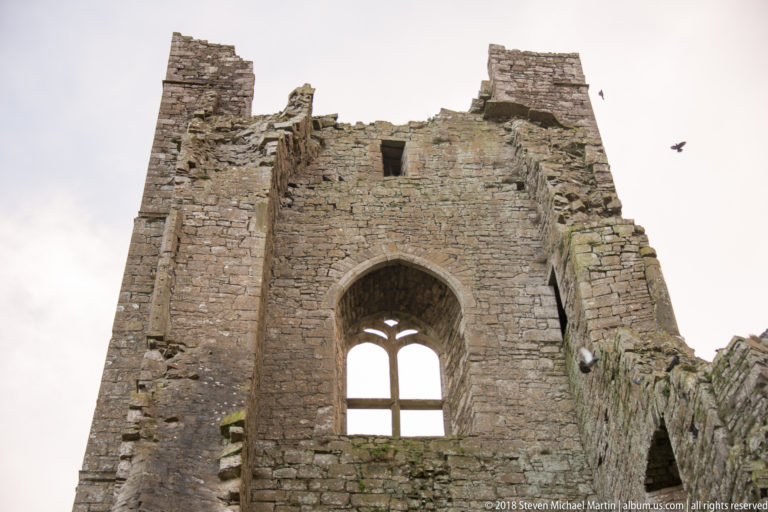 Tall ruined stone gable with a large pointed-arch window and surviving tracery against a pale sky.