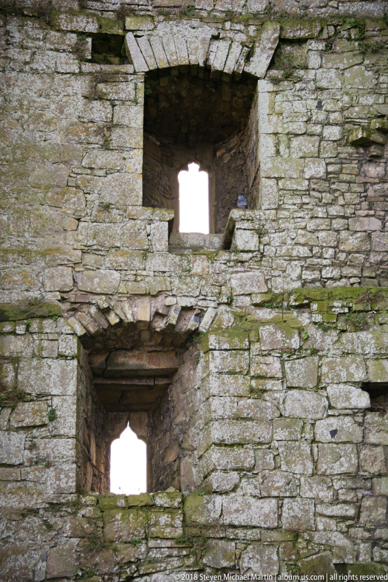 Two deep rectangular openings stacked in a thick weathered stone wall with daylight visible beyond.