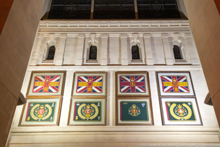 Two rows of framed military-style standards and badges mounted high on a pale cathedral wall.
