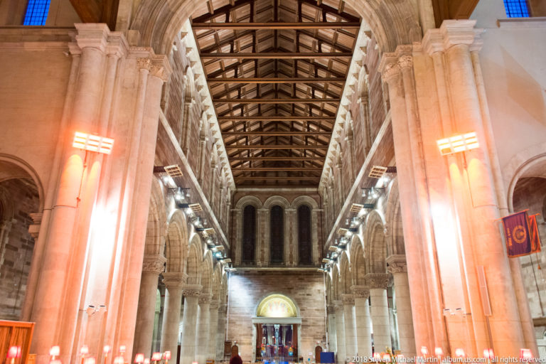 Long cathedral nave lined with stone arcades beneath an exposed timber roof, viewed toward the far end.