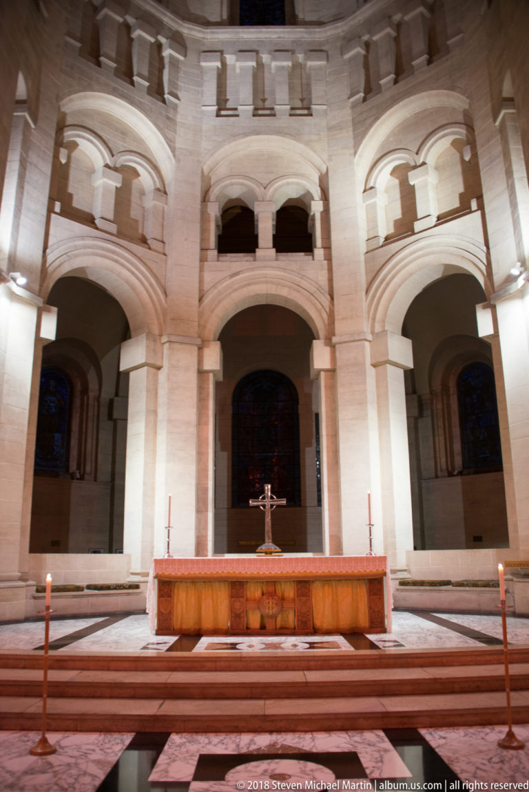 Central wooden altar and cross set before tall pale-stone arches in a cathedral sanctuary.