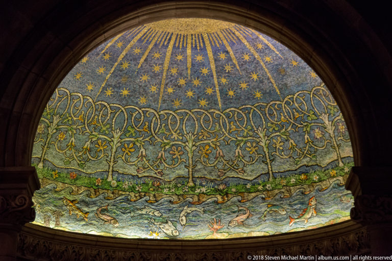 Semicircular blue-and-gold mosaic with stars above interlaced ornament, birds, animals, and landscape imagery.