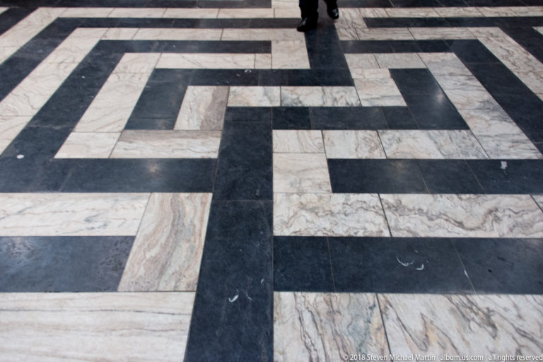 Black and veined white marble slabs arranged in a large interlocking geometric floor pattern.