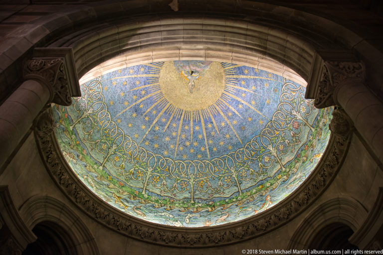 Curved apse mosaic with a white dove in a golden radiance above blue stars and interlaced ornament.