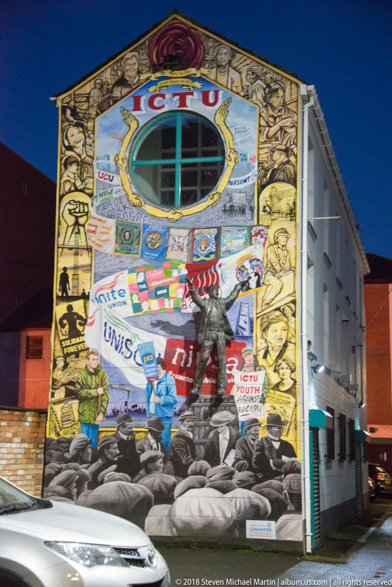 Multi-story building façade covered by a dense mural collage of faces, emblems, banners, and political references.