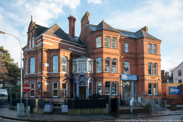 Large red-brick corner building with bay windows, chimneys, stone trim, and ground-floor hospitality signs.