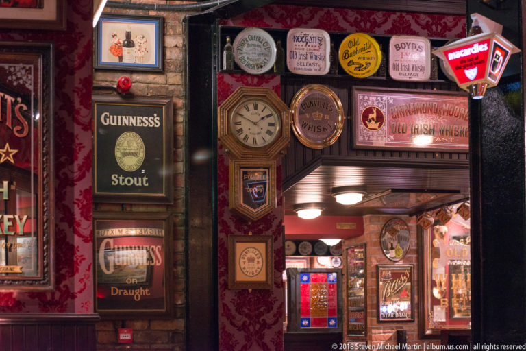 Belfast pub wall crowded with Guinness signs, whiskey plaques, a clock, and small illuminated advertisements.
