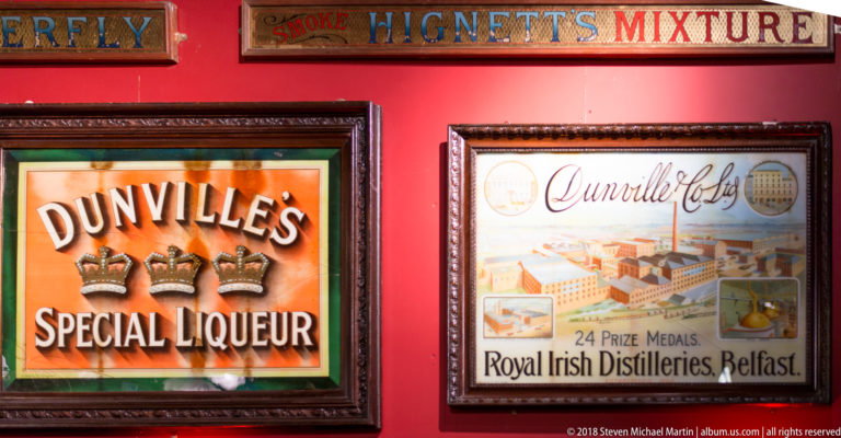 Framed Dunville’s Special Liqueur and Royal Irish Distilleries Belfast advertisements on a red pub wall.