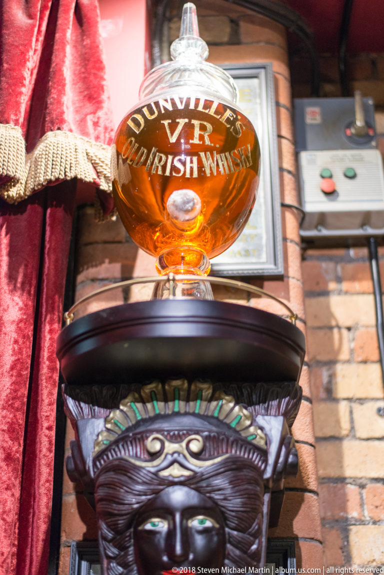 Round Dunville’s VR Old Irish Whisky glass display on an ornate dark pedestal inside a Belfast pub.