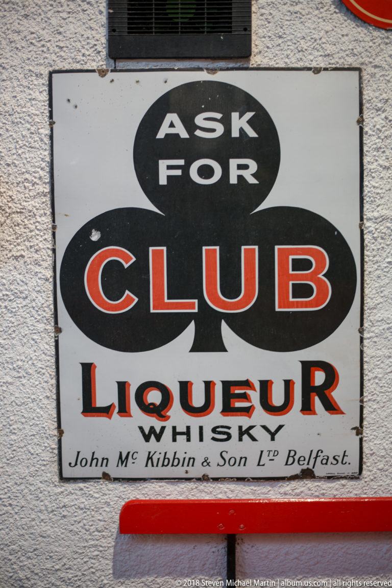 White enamel sign reading Ask for Club Liqueur Whiskey, John McKibbin & Son Ltd Belfast, with black club symbol.