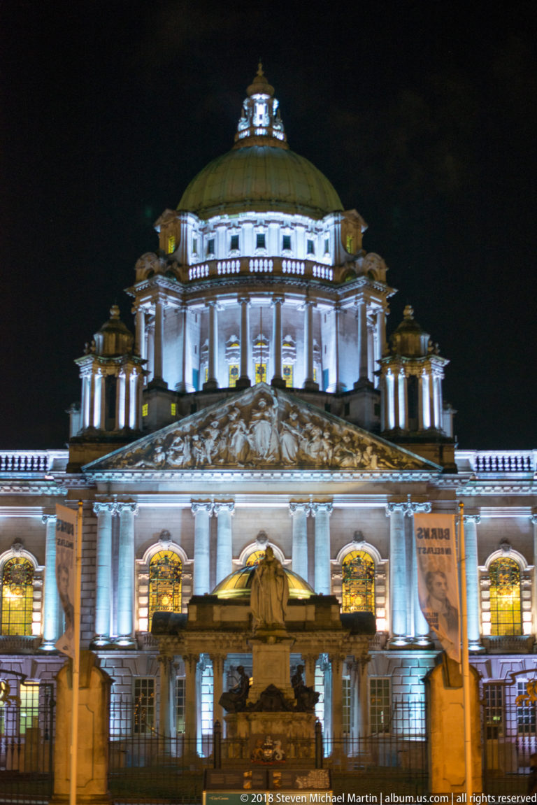 Illuminated central façade and copper-clad dome of Belfast City Hall at night, viewed frontally above the main entrance.
