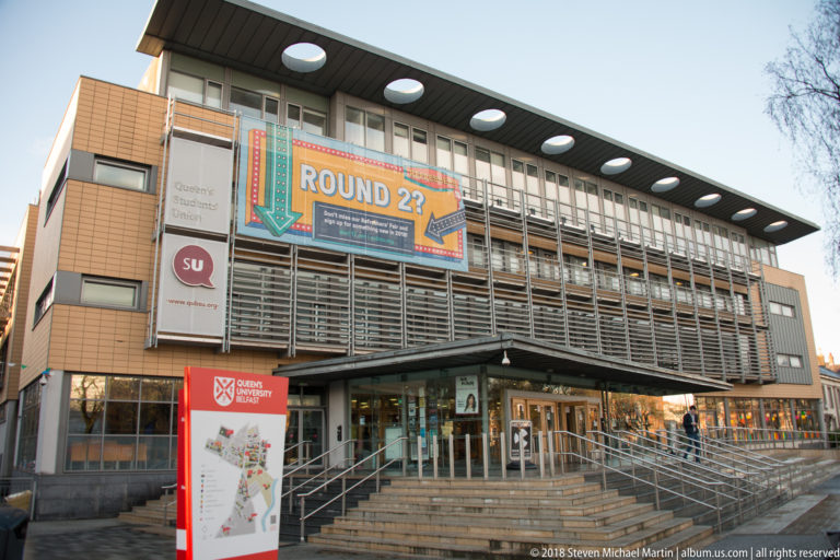 Modern Queen’s University Students’ Union façade with metal louvers, broad steps, university signage, and a large banner.