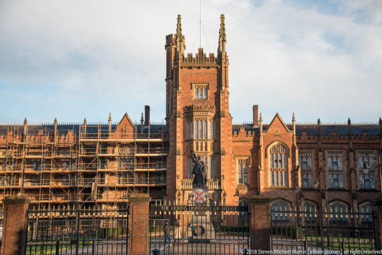 Front view of Queen’s University Belfast’s red-brick Lanyon Building, with central tower, iron gate, and scaffolding on one wing.